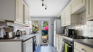 Una cocina con alacenas blancas, una cafetera, una estufa y vista al patio trasero.