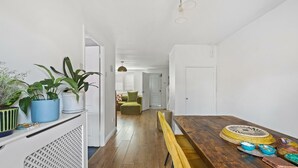 Un pasillo estrecho con una mesa de comedor de madera, plantas en macetas y vistas a una sala de estar con un sofá verde.