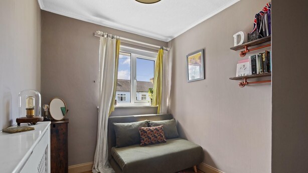 Una habitación pequeña y acogedora con ventana, un sofá, una estantería y un espejo.