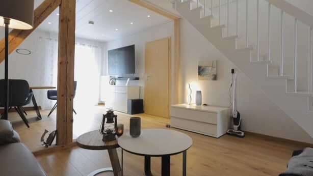 Una sala de estar moderna con una escalera, un comedor y una cocina al fondo.