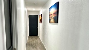 A hallway with a wooden floor, white walls, and two framed pictures on the right wall. - Cozy 2-bedroom house in gorgeous Carson with AC for relaxing stays (Carson)