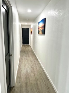 Un couloir avec un plancher en bois, des murs blancs et deux tableaux encadrés sur le mur de droite.