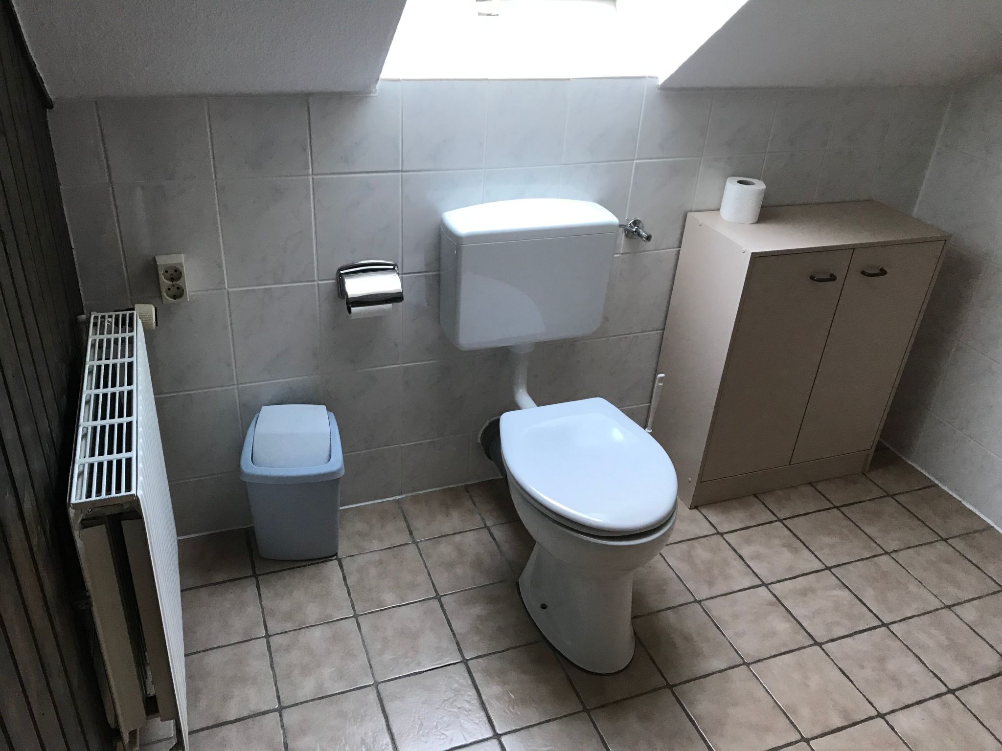 Un baño pequeño con inodoro, un bote de basura, dispensador de toallas de papel y un armario.