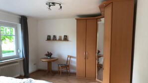 Quarto com cama, guarda-roupa de madeira, uma pequena mesa com cadeira e prateleira com quadros.