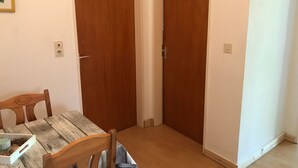 Um quarto com uma mesa e cadeiras de madeira, duas portas de madeira e uma parede branca com tomada.