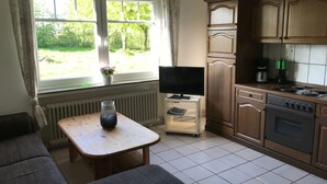 Uma cozinha compacta com área de refeições, uma TV sobre um suporte pequeno e uma janela com vista para vegetação.