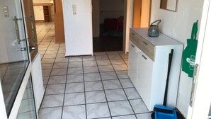 A narrow hallway with a tiled floor, a white refrigerator, and a blue trash bin. - Große Wohnung in Nesse mit Garten und Terrasse by Interhome (Nessmersiel)
