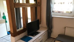 A small room with a TV on a wooden stand, a desk with drawers, a chair, and a window with curtains. - Große Wohnung in Nesse mit Garten und Terrasse by Interhome (Nessmersiel)