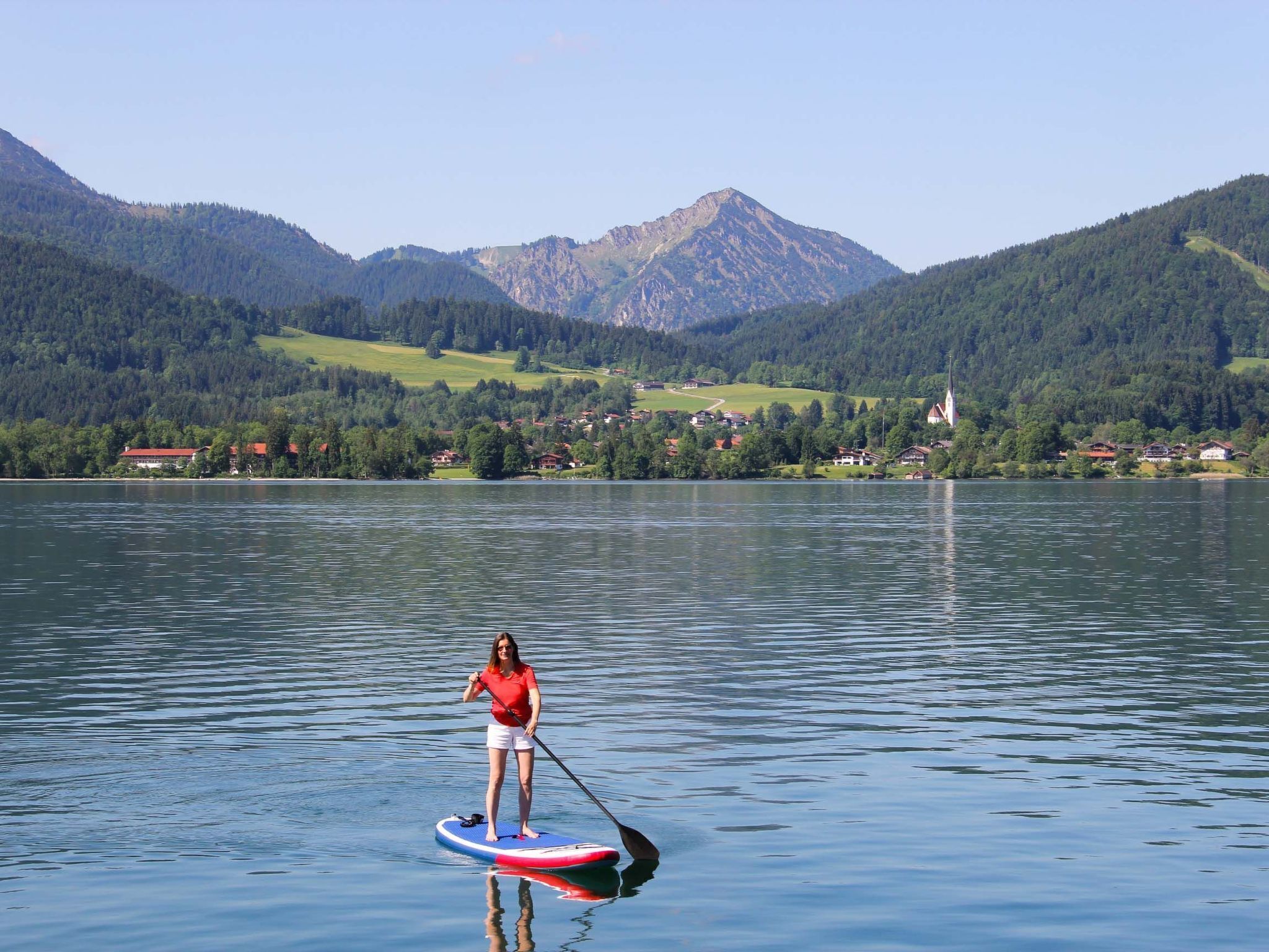 A woman paddleboarding on a calm lake with a mountainous backdrop.