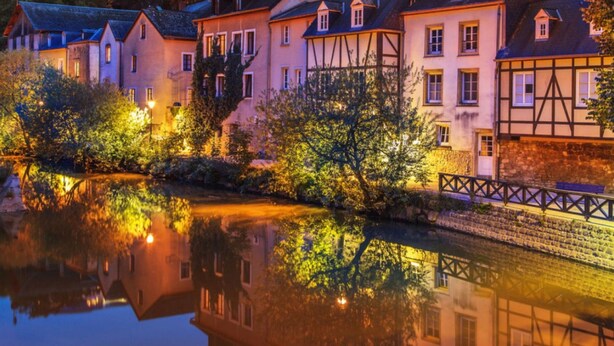 Eine Flussstadt mit traditioneller Bebauung, einer Brücke und einer Burg im Hintergrund.