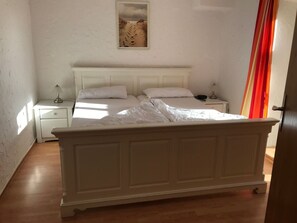 A bedroom with a large bed, a nightstand, a lamp, and a painting on the wall. - für vier Personen im Erdgeschoss by Interhome (Nessmersiel)
