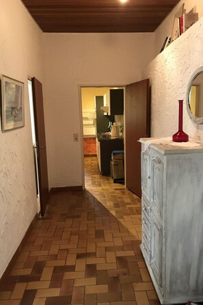 A hallway with a herringbone floor pattern, a white cabinet with a red vase, and a framed picture on the wall. - für vier Personen im Erdgeschoss by Interhome (Nessmersiel)