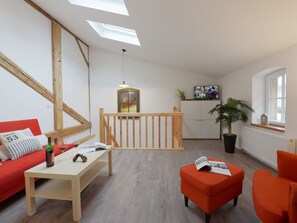 Ein modernes Wohnzimmer mit einer Holztreppe, einem roten Sofa, einem Holztisch und einem hellen Fenster.