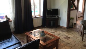 Ein Wohnzimmer mit einer Couch, einem Couchtisch, einem Fernseher und einem Fenster mit Vorhängen.