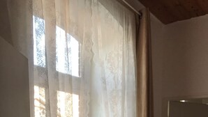 Ein Zimmer mit Fenster, das mit durchscheinenden Vorhängen bedeckt ist, einem Heizkörper darunter und einer geschlossenen Tür rechts.
