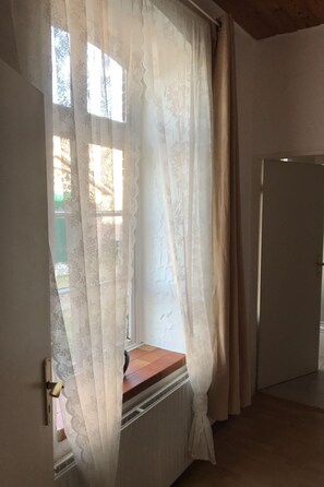 A room with a window covered by sheer curtains, a radiator below, and a closed door to the right. - für zwei Personen im Erdgeschoss by Interhome (Nessmersiel)