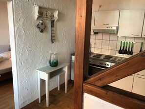 A kitchen with a stove, a small table, and a shelf with kitchen utensils. - für zwei Personen im Erdgeschoss by Interhome (Nessmersiel)