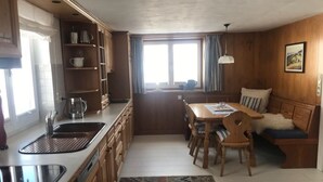 Una cocina compacta con zona de comedor, armarios de madera, un lavamanos y un ventanal con cortinas.