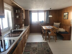 Eine kompakte Küche mit Essbereich, Holzschränken, einem Spülbecken und einem Fenster mit Vorhängen.