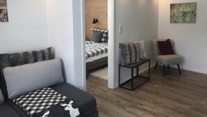 Una sala moderna con un sofá, un sillón y una cama al fondo.
