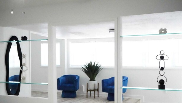 Un salón moderno con separador de vidrio, sillones azules, una planta en maceta y una decoración minimalista.