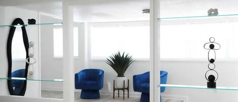 A modern living room with a glass partition, blue armchairs, a potted plant, and a minimalist decor.