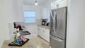 Una cocina moderna con armarios blancos, un refrigerador de acero inoxidable, encimeras de granito e iluminación colgante.