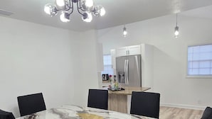 Un comedor moderno con una mesa de mármol y sillas negras, una cocina al fondo y una lámpara en el techo.