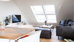 A modern loft apartment with a sloped ceiling, a large skylight, a flat-screen TV, a sofa, a dining table, and a coffee table. - Hochwertige, helle FeWo mit Meerblick am Deich by Interhome (Nessmersiel)