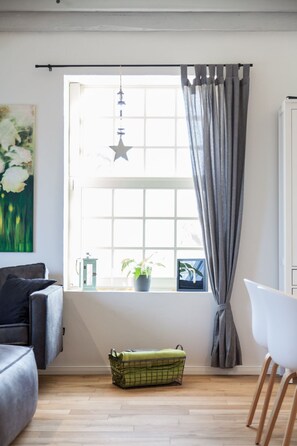 A room with a window, a hanging star ornament, a potted plant, a green basket, and a white chair. - Hochwertige, helle FeWo mit Meerblick am Deich by Interhome (Nessmersiel)