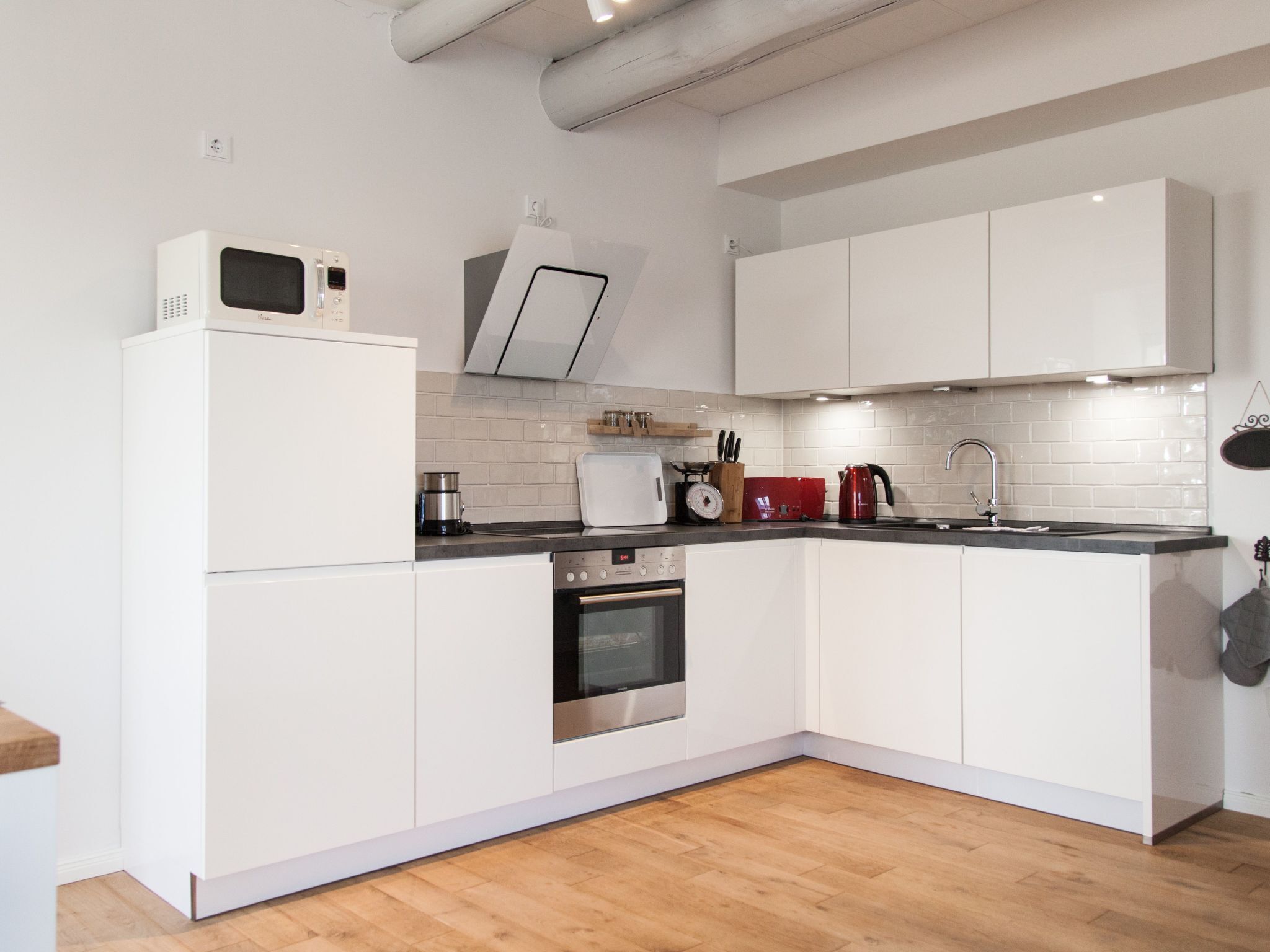 A modern kitchen with white cabinets, a stainless steel oven, a microwave, and a red kettle.