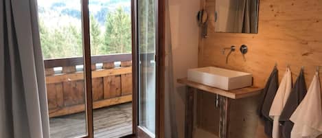 Un baño con tocador de madera, un espejo grande y vistas al exterior a través de una puerta corrediza de vidrio.