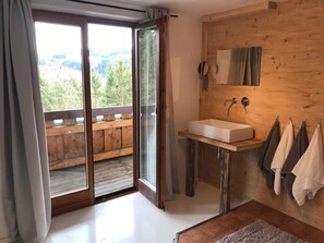 Une salle de bain avec un meuble-lavabo en bois, un grand miroir et une vue sur l’extérieur grâce à une porte-fenêtre coulissante.