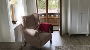 A room with a striped armchair, a wooden floor, a white wardrobe, and a view of a balcony with a wooden railing. - Kräuterhof-Ferienwohnung by Interhome (Missen-Wilhams)