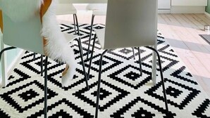 Une cuisine moderne avec des meubles blancs, des suspensions noires et un tapis à motifs.