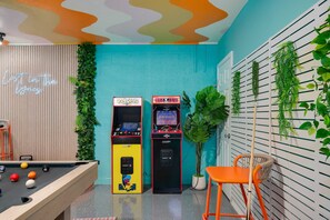 A pool table, arcade machines, a neon sign, and indoor plants.