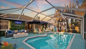 Un área de piscina con sillones de descanso, una chimenea y un porche cubierto.