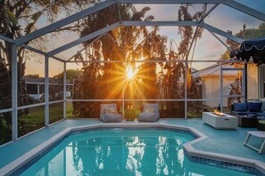 A pool area with a view of the sunset, two lounge chairs, and a fire feature.