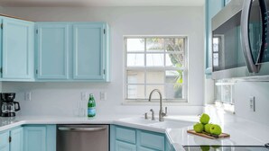 Una cocina moderna con armarios azul claro, lavavajillas de acero inoxidable, un fregadero con grifo y un ventanal que proporciona luz natural.