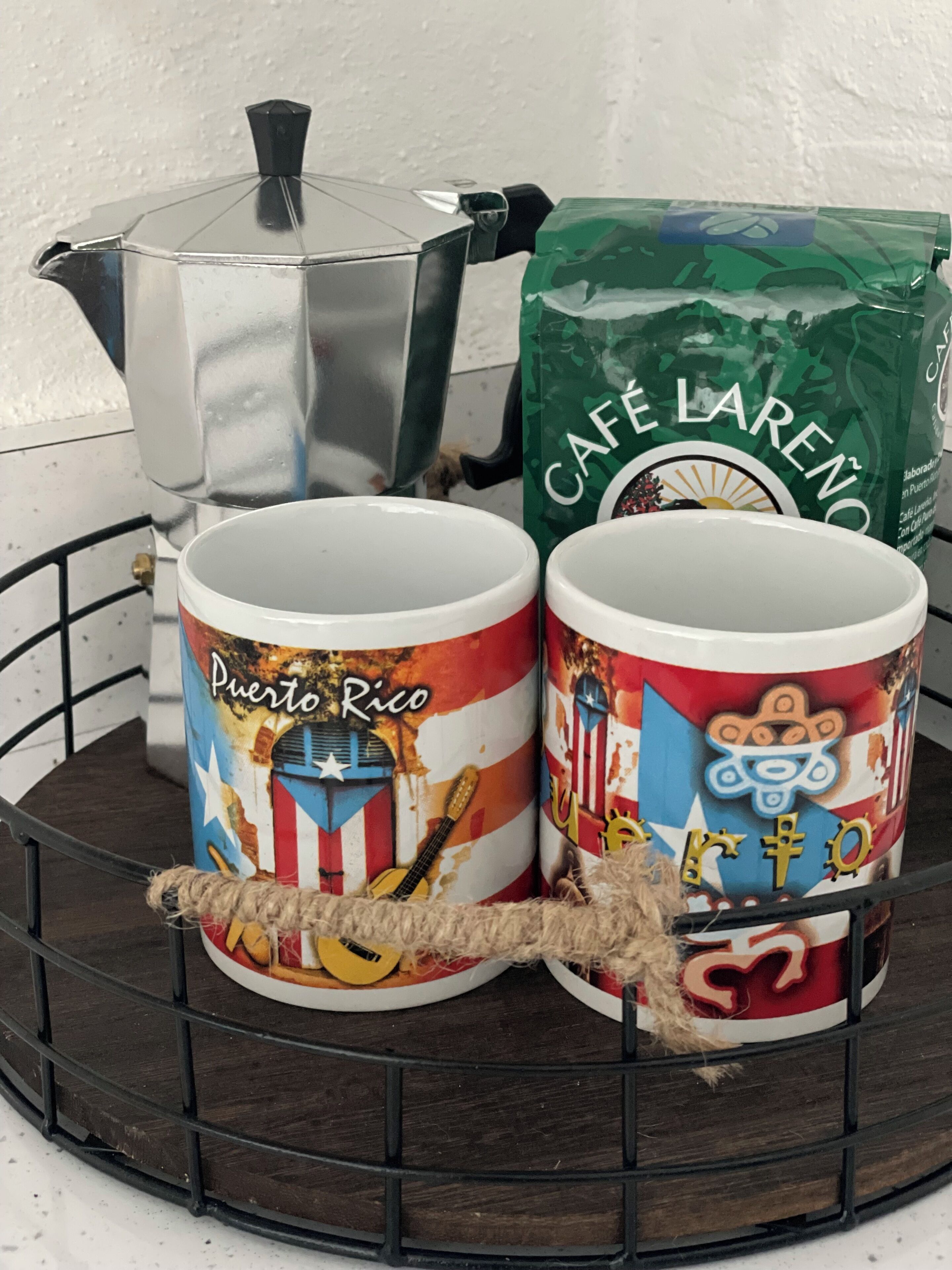 Two coffee mugs with Puerto Rico designs, a silver coffee pot, and a bag of Café Lareno coffee.