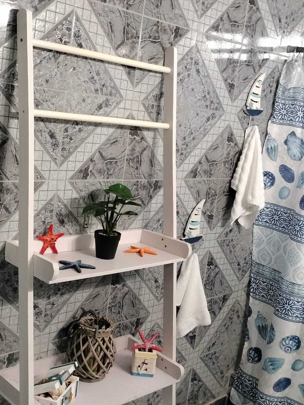 A bathroom with a white shelf unit, a potted plant, starfish decorations, and a towel rack with a blue and white patterned towel.