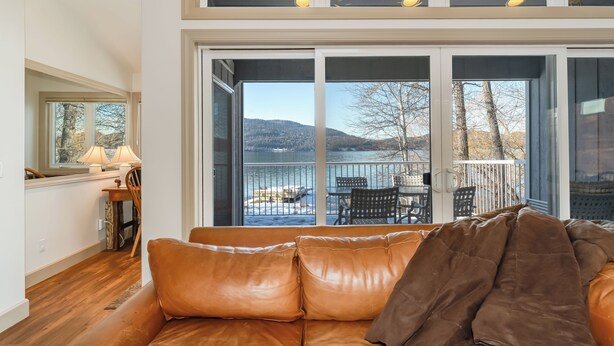 A cozy living room with a leather sofa, a dining area with a table and chairs, and large sliding glass doors leading to a balcony with a scenic view. - New! 30-Day Min | Whitefish Lake Views | 3BR Condo w/ Deck Near Downtown (Whitefish)