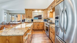 A modern kitchen with wooden cabinets, stainless steel appliances, and a granite countertop. - New! 30-Day Min | Whitefish Lake Views | 3BR Condo w/ Deck Near Downtown (Whitefish)