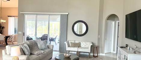 A spacious living room with a sofa, armchairs, a coffee table, and a television.