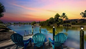 A poolside area with three chairs and a view of a sunset over a body of water. - Luxury Waterfront Home-Heated Pool-Dock-Sleeps 10 (Cape Coral)