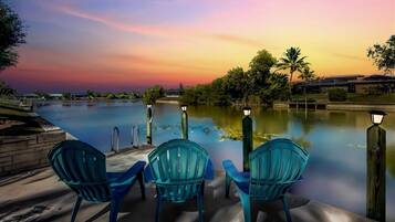 Zona junto a la piscina con tres sillas y vista a un atardecer sobre el agua.