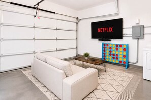 A modern living room with a white sofa, a coffee table, a TV mounted on the wall, and a colorful game board.