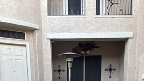 An outdoor patio area with a wicker chair, a bench, potted plants, a trash can, and a patio heater. - Welcoming studio with AC in charming Goodyear (Goodyear)