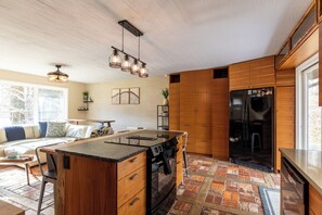 A modern kitchen with a central island, wooden cabinets, a black refrigerator, and a hanging light fixture. - Ski, Hike, and Relax by the Creek - Hot Tub, Creek Access, Sleeps 11 (Banner Elk)