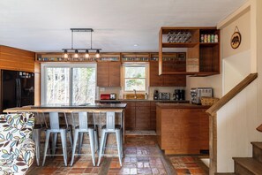 A kitchen with a central island, bar stools, wooden cabinets, a built-in wine rack, and a staircase. - Ski, Hike, and Relax by the Creek - Hot Tub, Creek Access, Sleeps 11 (Banner Elk)